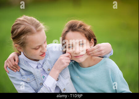 Blonde Mädchen ziehen Lächeln auf den kaukasischen Freund Gesicht mit beiden Händen, die versucht, Ihr glücklich lächelnde im Freien zu machen Stockfoto