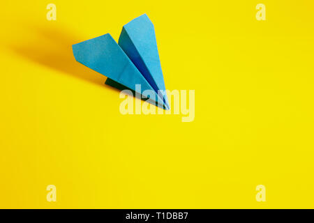 Blaues Papier Flugzeug auf einem gelben Hintergrund, mit langen Schatten Stockfoto