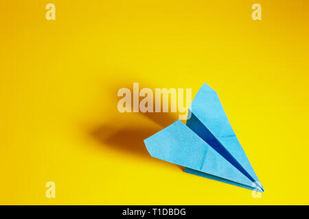 Blaues Papier Flugzeug auf einem gelben Hintergrund, mit langen Schatten Stockfoto