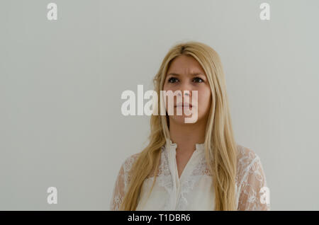 Verärgert junge blonde Frau bläst die Backen in Unzufriedenheit, hebt die Augenbrauen und Runzelt Gesicht, bringt negative Emotionen. Junges Mädchen mit grünen Augen ein Stockfoto