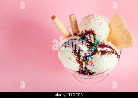 Vanille Eis in Glas Schale mit Schokoladensauce, streuten besprüht und Waffeln auf rosa Hintergrund Stockfoto
