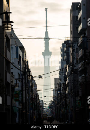 Die Skytree Türme über Tokio, Japan. Von einer engen Gasse der Turm ist nur eine dunkel Drohende Schatten am frühen Morgen Licht sehen durch den Smog gesehen Stockfoto