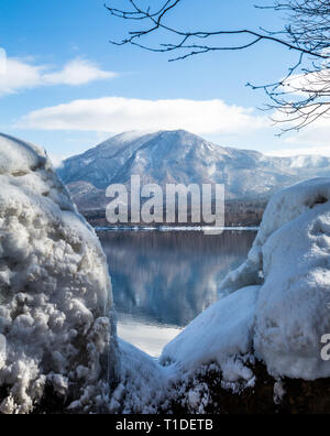 Schnee auf Felsen und unter Eis bilden. Die fernen Gipfel ist in der flachen See Wasser wider. Stockfoto