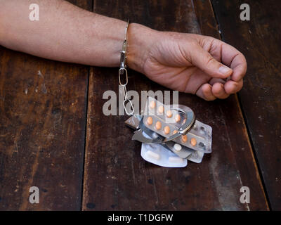 Ein Mann in Handschellen auf eine Handvoll Pillen Tabletten. Drogensucht Konzept Stockfoto