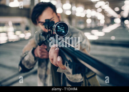 Ein Bild, wenn Erwachsene dunkelhaarigen Mann Ziel nehmen. Er ist mit Paintball Gewehr für das. Er spielt Paintball Spiel. Stockfoto