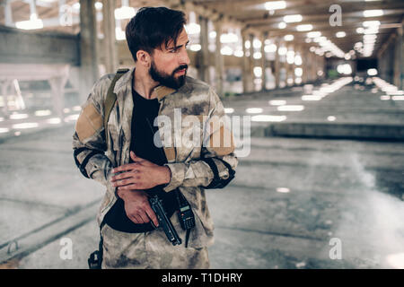 Sorgfältige und ernster junger Mann ist auf der Suche nach rechts. Er trägt spezielle Uniform. Auch Kerl hat kleine Pistole in seiner rechten Hand. Mann steht in großen Stockfoto