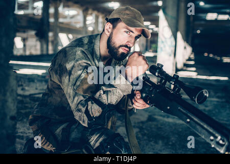 Ruhig und friedlich Soldat Sucht gerade nach vorn. Er wartet. Junger Mann sitzt mit einem Knie. Kerl trägt Uniform. Stockfoto