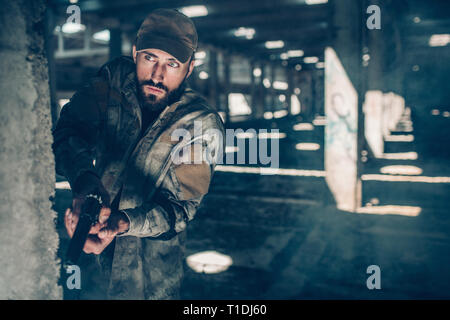 Achten Mann sucht gerade nach vorn. Er steht hinter Spalte in einem großen Hangar. Krieger ha eine kleine schwarze Pistole. Er ist bereit, zu jeder Zeit zu schießen. Stockfoto