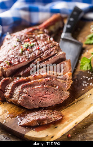 Frisch gegrillten Tomahawk Steak auf schiefer Teller mit Salz, Pfeffer, Rosmarin und Petersilie Kräuter. In Scheiben geschnittene Stücke von saftigen Rindersteak Stockfoto