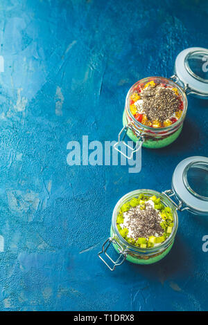 Zwei Chia Samen Pudding mit Matcha Grüntee, Kiwi und Müsli, orange in Gläsern auf Dunkelblauem konkreten Hintergrund. Gesundes Frühstück. Stockfoto