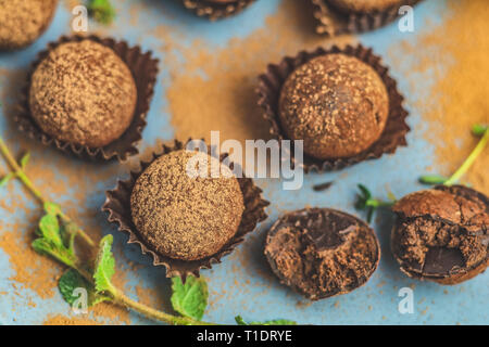 Kakao Kugeln, handgemachte Schokolade Kugeln Kuchen in einem blauen Fach, mit Kakaopulver, frischer Minze und Thymian auf dunkelblauem Hintergrund sprengte die Betonoberfläche Stockfoto