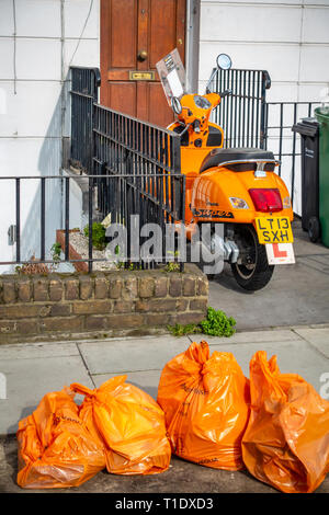 Rückansicht eines hellen orange motor scooter außerhalb eines Hauses Tür mit vier orange Recycling Taschen vor dem Fahrrad und Haus geparkt Stockfoto