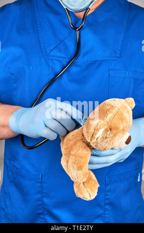 Arzt in der blauen Uniform und Latex Handschuhe mit einem braunen Teddybär, Kinderarzt behandelt ein Spielzeug Stockfoto