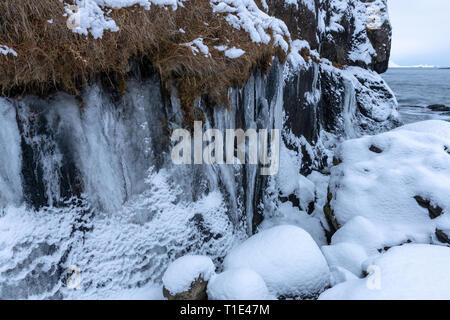 Eiszapfen und Felsen im Schnee am Meer im südlichen Island Stockfoto