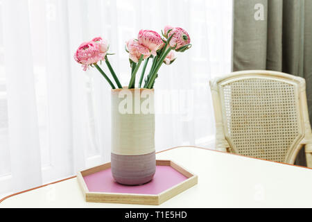 Rosa Blumen in einem lila Vase gegen ein weißes Fenster. Aster Blumenstrauß in der Vase auf dem Tisch. Stockfoto