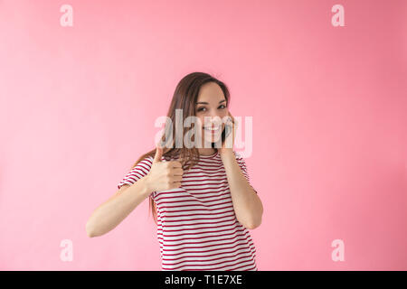 Positive schönen jungen Mädchen verwendet ein Mobiltelefon, und zeigt mit dem Daumen nach oben Zeichen Bedeutung OK. Stockfoto