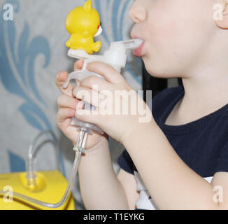 Das Kind macht einatmen. Der Junge hält in seiner Hand ein Inhalationsgerät für die Behandlung von Atemwegserkrankungen. Einatmen. Die Behandlung von Kindern. Die Stockfoto