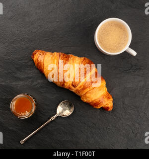 Ein Foto von einem Croissant mit einer Tasse Kaffee und einem marmeladenglas auf einem schwarzen Hintergrund mit Kopie Raum Stockfoto