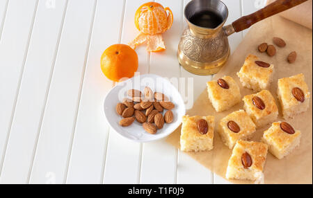 Stücke (Basbousa namoora) traditionelle arabische Grieß Kuchen mit Mandeln Mutter und Sirup, orange und Cooper jezva. Kopieren Sie Platz. Selektive konzentrieren. Ansicht von oben. Stockfoto