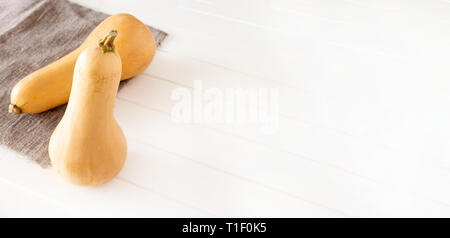 Zwei organischen butternut squash Leinwand Serviette weiß Holz- Hintergrund. Herbst Ernte oder Kochen Konzept. Banner Größe. Stockfoto