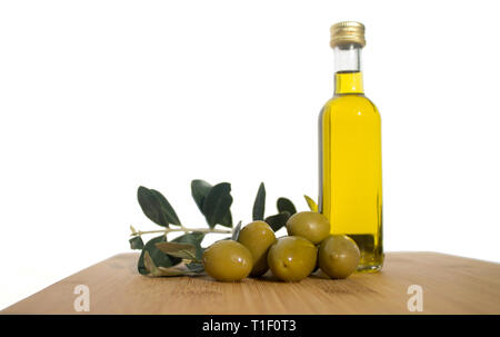 Glasige Flasche Olivenöl mit einer Gruppe von grünen glänzenden Oliven und Brunches mit treibt auf dem hölzernen Tisch auf weißem Hintergrund entfernt Stockfoto