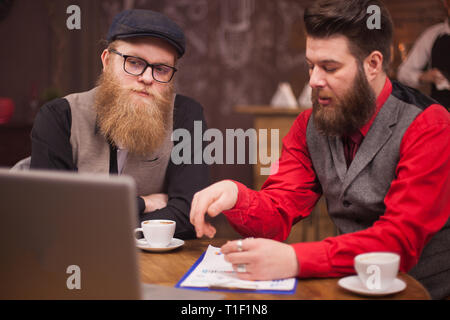 Schöne bärtige Männer in Business Video Anruf auf seinem Laptop in einem Café. Kaffeetasse. Laptop. Erfolgreiche Männer. Stockfoto