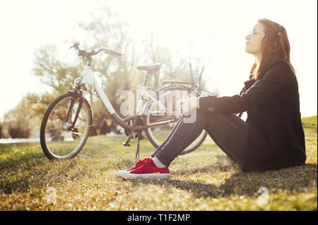 Junge Frau mit dem Fahrrad entspannt sitzen auf Gras im Natur Park Stockfoto
