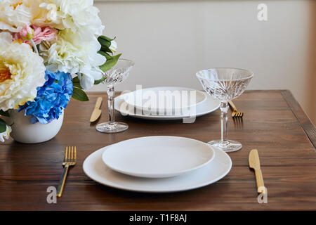 Platten, goldenen Messern und Gabeln mit Kristallgläsern und Blumen in Vase auf hölzernen Tisch im Restaurant Stockfoto