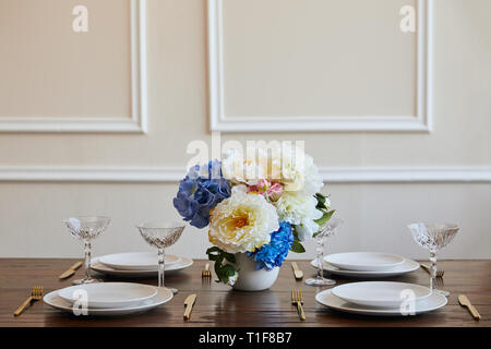 Weiße Platten, goldenen Messern und Gabeln, Kristallgläser und Blumen in Vase auf hölzernen Tisch im Restaurant Stockfoto
