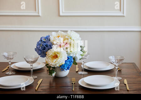 Teller, Messer und Gabeln, Kristallgläser und Blumenstrauß in weiße Vase auf hölzernen Tisch im Restaurant Stockfoto