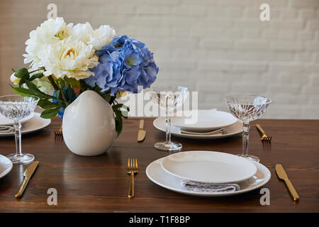 Teller, Messer und Gabeln, Kristallgläser und Blumenstrauß in Vase auf hölzernen Tisch im Restaurant Stockfoto