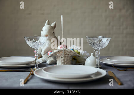 Weiß Teller, Besteck, Kristallgläser, dekorative bunnie und Korb mit bemalte Eier auf den Tisch zu Hause. Stockfoto