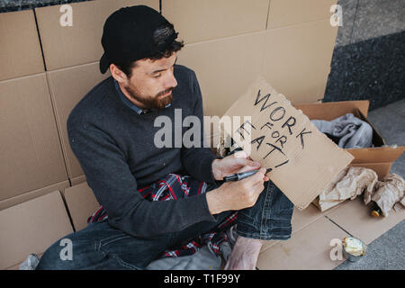 Arbeitslose Mann sitzt auf dem Boden und schreiben die Wörter für Essen auf dem Stück Papier arbeiten. Mann ist auf der Suche nach einem Job. Er hofft, dass jemand helfen Stockfoto