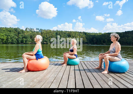 Gruppe von älteren Frauen an Rehabilitation Rückentraining mit Gymnastikball am See im Sommer Stockfoto