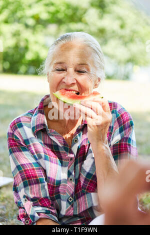 Hungrig senior Frau isst eine Wassermelone im Park auf einer Reise im Sommer Stockfoto