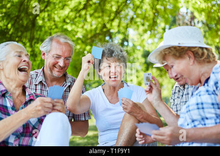 Senior Freunden Karten in einem Turnier in der Freizeit im Garten oder Park Stockfoto