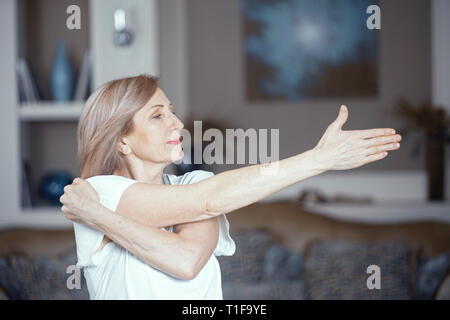 Eine 50 Jahre alte Frau übt Yoga zu Hause im Wohnzimmer. Stockfoto