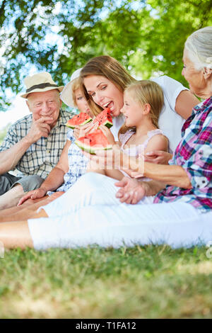 Erweiterte Familie mit Kind und Großeltern bei einem Picknick im Sommer und essen Melonen Stockfoto