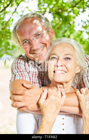 Gerne älteres Paar liebevoll umarmt einander im Sommer in der Sonne in der Natur Stockfoto