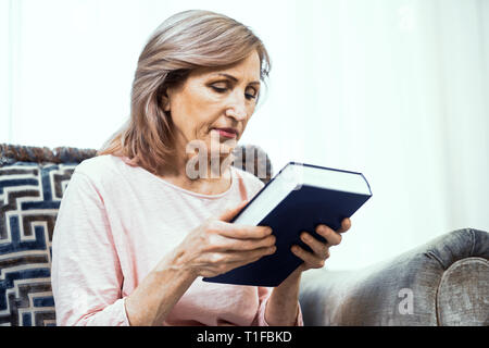 Frau mittleren Alters saß auf dem Sofa und halten Bibel Stockfoto