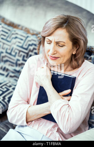 Frau mittleren Alters saß auf dem Sofa und halten Bibel Stockfoto