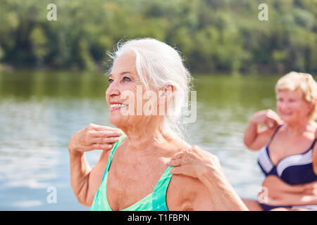 Vital senior Frau tun einer Gymnastik Übung für die Rückseite, die am See im rehab Stockfoto