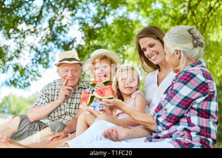 Erweiterte Familie mit Kind und Großeltern essen Melone im Sommer im Garten Stockfoto