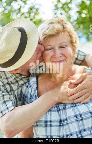 Älterer Mann zärtlich umarmt und küsst seine Frau im Sommer auf Urlaub in der Natur Stockfoto