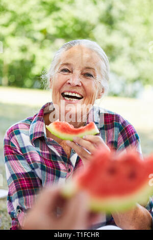 Freundliche ältere Frau essen Melone im Park im Sommer auf einer Reise Stockfoto