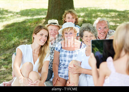 Frau mit Tablet. Computer nimmt Bild der erweiterten Familie mit Kind und Großeltern im Park Stockfoto