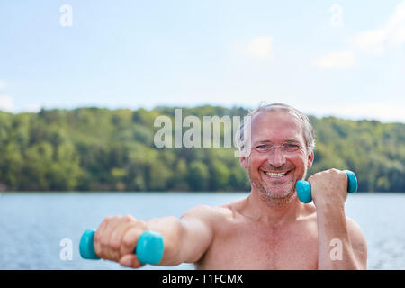 Vital Senior in der Natur am Ufer des Sees Züge mit Hanteln für Fitness und Kraft Stockfoto