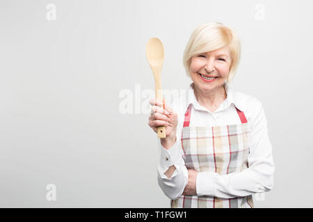 Ältere Frau, und halten einen Löffel. Sie ist eine gute Hausfrau. Sie mag leckeres Essen zu kochen. Auf weissem Hintergrund. Stockfoto