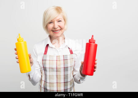 Tolles Bild der alten Frau mit zwei Flaschen sauses in den Händen. Sie möchten einen Leckerbissen für Ihren Geliebten zu kochen. Auf weissem Hintergrund. Stockfoto