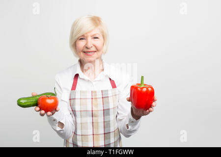 Eine schöne reife Frau mit einem roten Pfeffer in der linken Hand und beide Tomate und Gurke in der rechten Hand. Sie liebt es, verschiedene Salate, um zu kochen oder zu Stockfoto